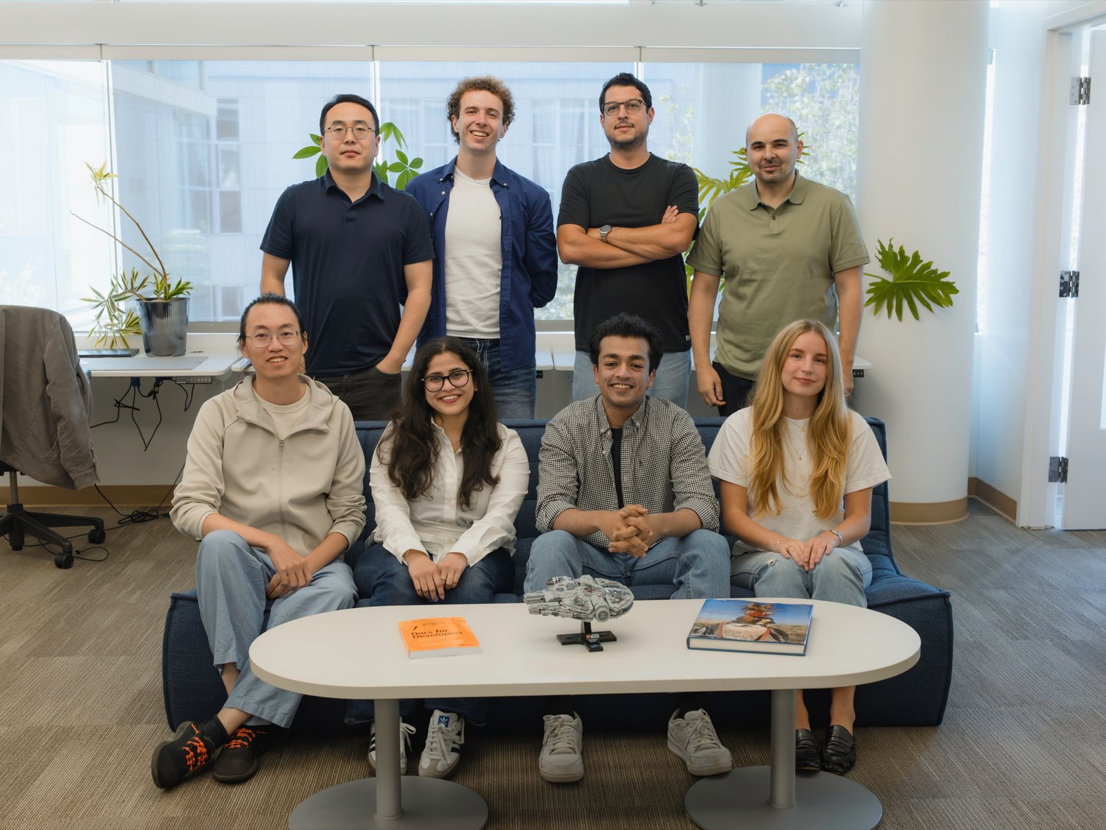 The Falconer team in the office, four people standing behind four people seated on a couch.